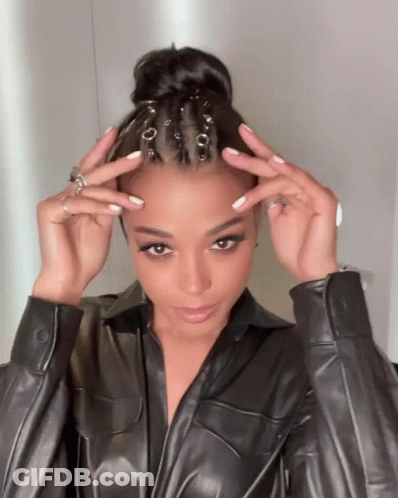 A Woman Wearing A Black Leather Jacket Holds Her Hair Up In A Bun GIF