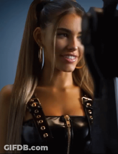 A Woman Wearing A Black Leather Top And Hoop Earrings Smiles For The Camera GIF