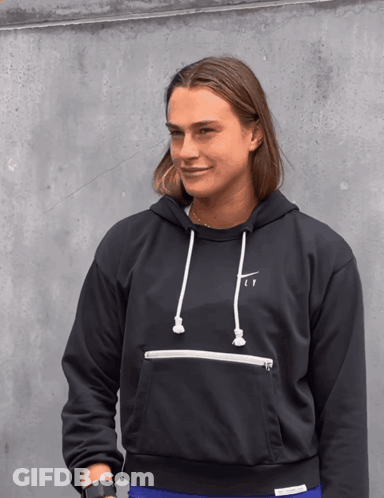 A Woman Wearing A Black Nike Hoodie Stands In Front Of A Grey Wall GIF