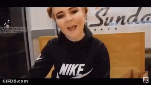 A Woman Wearing A Black Nike Sweatshirt Is Sitting In Front Of A Sign That Says Sunda . GIF