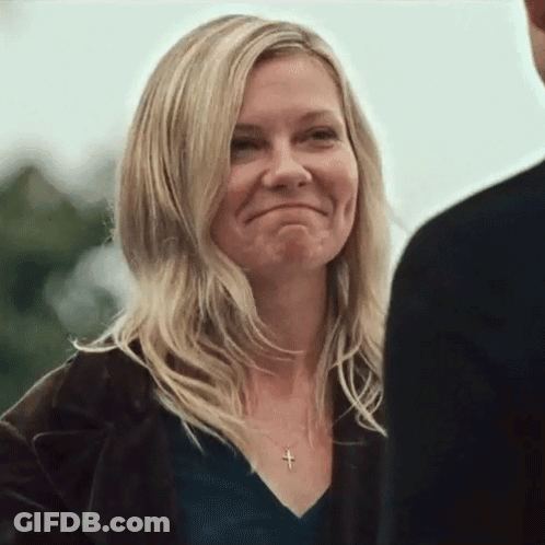 A Woman Wearing A Black Shirt And A Cross Necklace Is Smiling While Looking At A Man . GIF