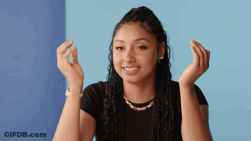 A Woman Wearing A Black Shirt And A Gold Necklace Is Smiling With Her Hands In The Air GIF