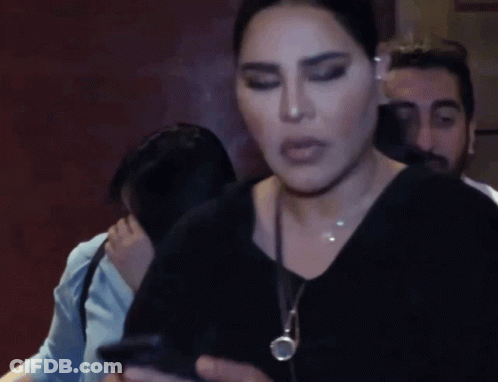 A Woman Wearing A Black Shirt And A Necklace Looks At The Camera GIF