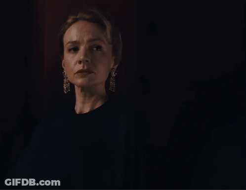 A Woman Wearing A Black Shirt And Earrings Looks At The Camera In A Dark Room GIF