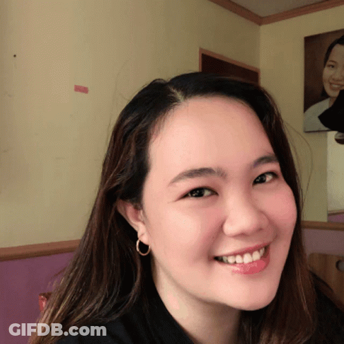 A Woman Wearing A Black Shirt And Hoop Earrings Smiles GIF