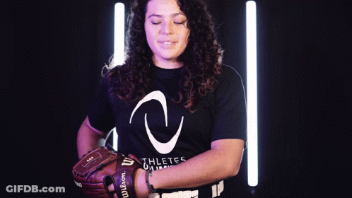 A Woman Wearing A Black Shirt That Says Athletes On It Is Holding A Wilson Baseball Glove GIF