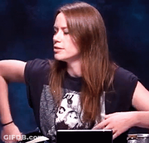 A Woman Wearing A Black Shirt With A Picture Of A Skull On It Is Sitting At A Table With A Laptop . GIF