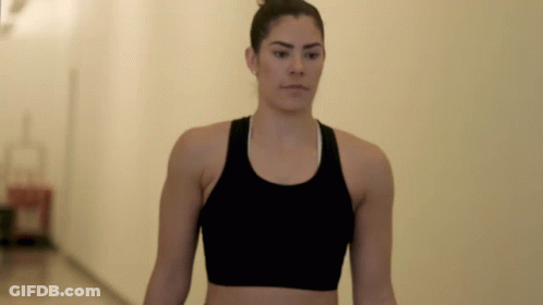 A Woman Wearing A Black Sports Bra Is Walking Down A Hallway GIF