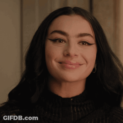 A Woman Wearing A Black Sweater And Hoop Earrings Smiles For The Camera GIF