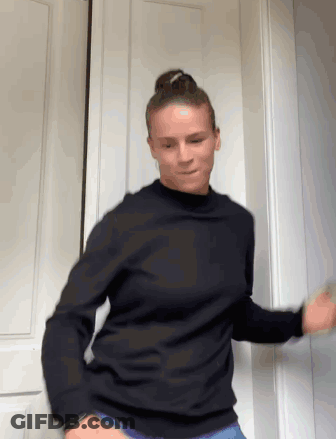 A Woman Wearing A Black Sweater Is Dancing In Front Of A Door GIF