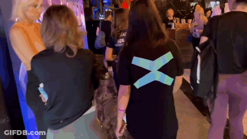 A Woman Wearing A Black T-Shirt With A Blue X On The Back GIF