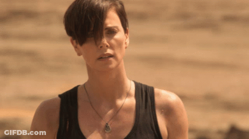 A Woman Wearing A Black Tank Top And A Necklace With A Pendant On It GIF