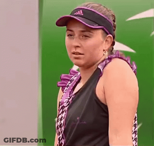 A Woman Wearing A Black Tank Top And A Purple Visor Is Standing In Front Of A Green Wall . GIF