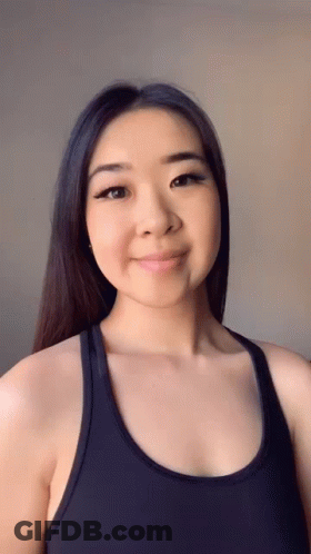 A Woman Wearing A Black Tank Top Is Smiling For The Camera GIF