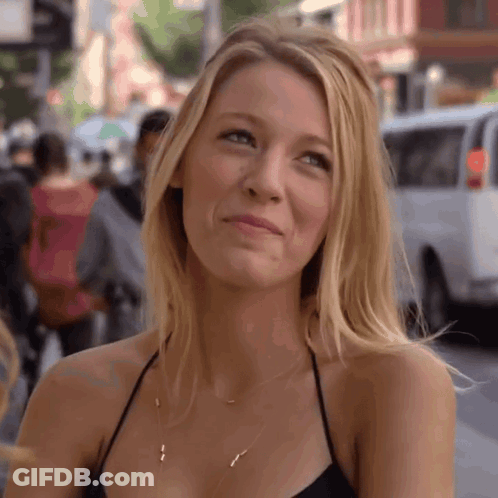 A Woman Wearing A Black Top And A Gold Necklace Smiles GIF