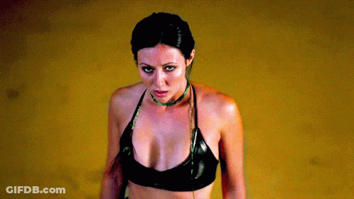 A Woman Wearing A Black Top And A Green Necklace GIF