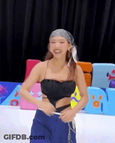 A Woman Wearing A Black Top And Blue Pants Is Standing In Front Of A Playground . GIF