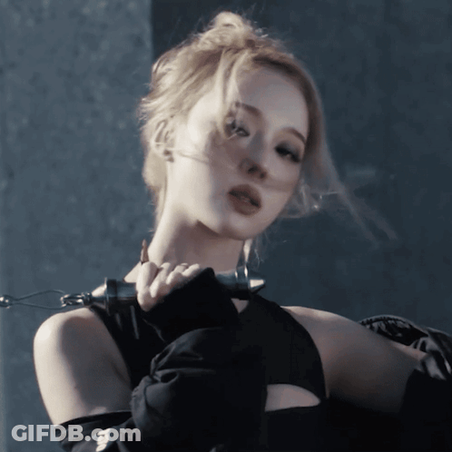 A Woman Wearing A Black Top And Gloves Holds A Chain Around Her Neck GIF