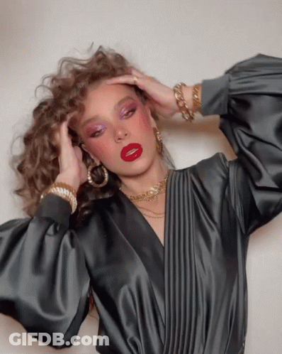 A Woman Wearing A Black Top And Red Lipstick Holds Her Hair GIF