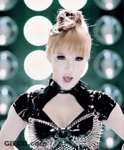A Woman Wearing A Black Top With Spikes On It Is Standing In Front Of A Bunch Of Lights . GIF