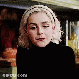 A Woman Wearing A Black Turtleneck And A Headband Looks At The Camera GIF