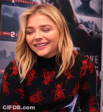 A Woman Wearing A Black Turtleneck With Red Bees On It GIF