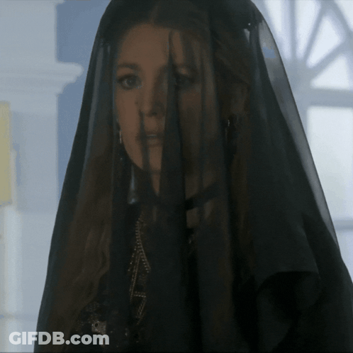 A Woman Wearing A Black Veil Is Standing In Front Of A Window GIF