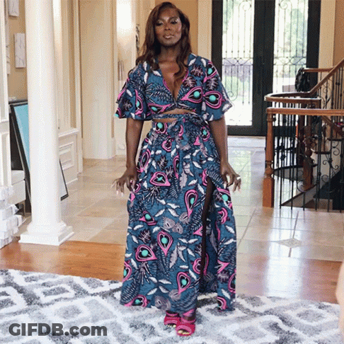 A Woman Wearing A Blue And Pink Dress Is Standing In A Hallway GIF