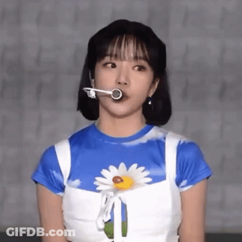 A Woman Wearing A Blue And White Shirt With A Daisy On It Is Holding A Microphone In Her Mouth . GIF