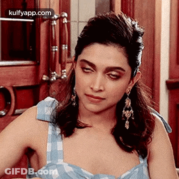 A Woman Wearing A Blue Dress And Earrings Is Sitting In Front Of A Door . GIF