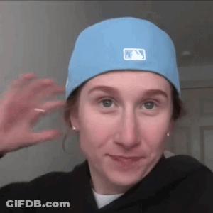 A Woman Wearing A Blue Hat And A Black Hoodie Is Waving At The Camera . GIF