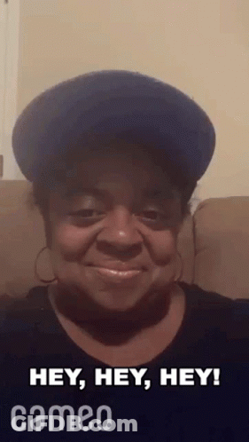A Woman Wearing A Blue Hat And Earrings Is Sitting On A Couch And Smiling . GIF