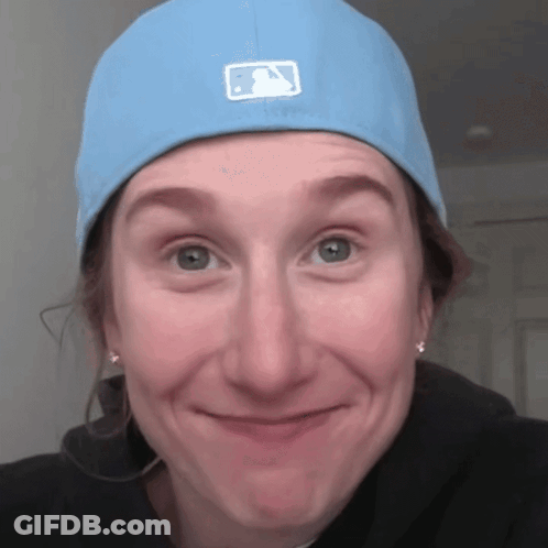 A Woman Wearing A Blue Hat With A Baseball Logo On It Makes A Funny Face GIF