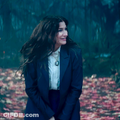 A Woman Wearing A Blue Jacket And White Shirt Is Standing In A Forest . GIF