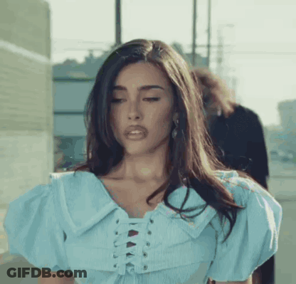 A Woman Wearing A Blue Lace Up Top Is Standing On A Sidewalk . GIF