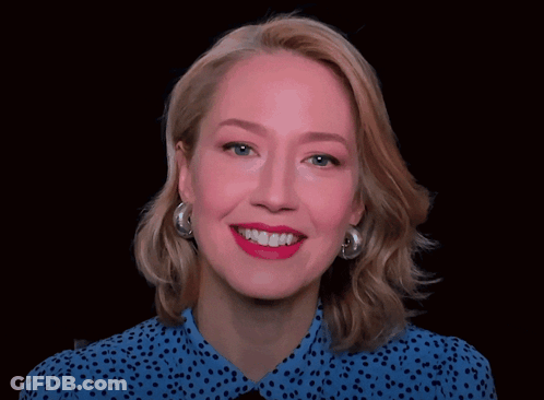 A Woman Wearing A Blue Polka Dot Shirt And Silver Hoop Earrings Is Smiling GIF