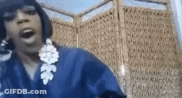 A Woman Wearing A Blue Robe And Earrings Is Standing In Front Of A Wicker Screen . GIF