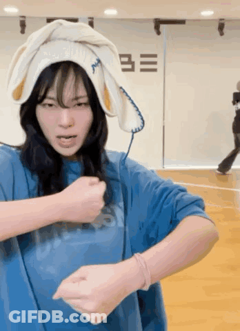 A Woman Wearing A Blue Shirt And A White Towel On Her Head Is Dancing . GIF