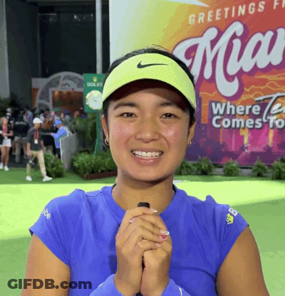 A Woman Wearing A Blue Shirt And A Yellow Nike Visor Smiles In Front Of A Miami Sign GIF