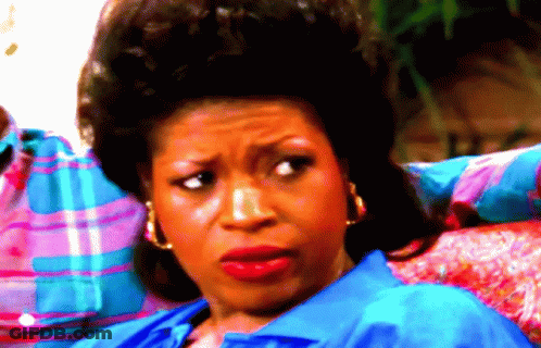 A Woman Wearing A Blue Shirt And Gold Hoop Earrings Looks At The Camera GIF