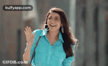 A Woman Wearing A Blue Shirt And Hoop Earrings Is Waving Her Hand . GIF