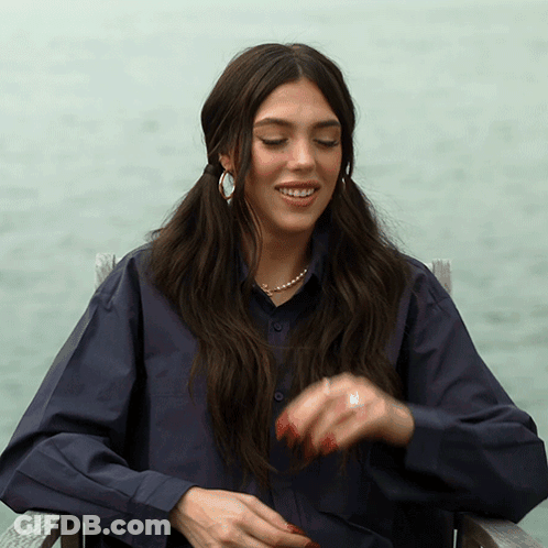 A Woman Wearing A Blue Shirt And Pearls Is Sitting In A Chair GIF