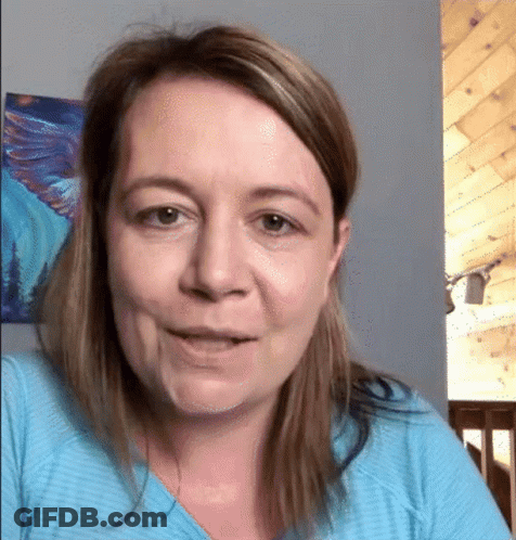 A Woman Wearing A Blue Shirt Is Smiling In Front Of A Painting On The Wall . GIF