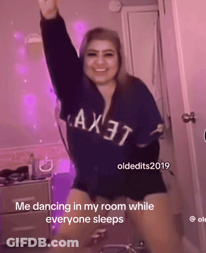 A Woman Wearing A Blue Shirt That Says Ax37 Is Dancing In A Room While Everyone Sleeps GIF