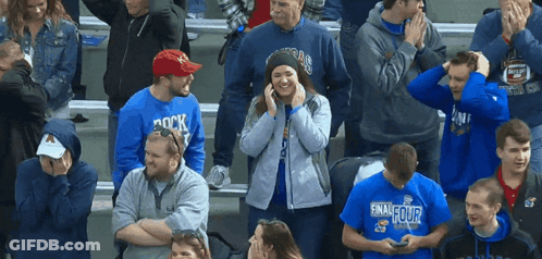 A Woman Wearing A Blue Shirt That Says Final Four Stands In A Crowd Of People GIF