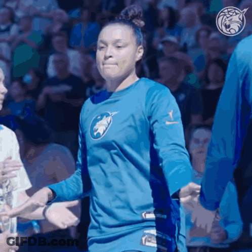A Woman Wearing A Blue Shirt With A Wolf On It Shakes Hands With Other People GIF