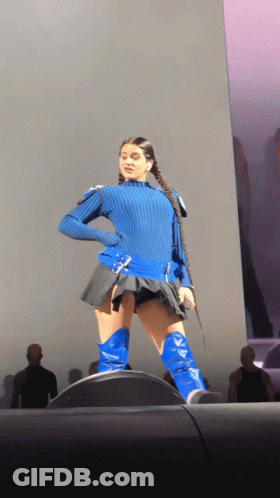 A Woman Wearing A Blue Sweater And Blue Boots Is Standing On A Stage GIF