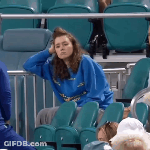 A Woman Wearing A Blue Sweatshirt That Says Silk Mills Sits In A Stadium GIF