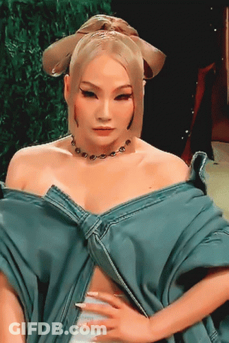 A Woman Wearing A Blue Top And A Necklace Is Looking At The Camera GIF