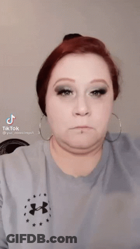 A Woman Wearing A Blue Under Armour Shirt Is Applying Makeup To Her Eye . GIF